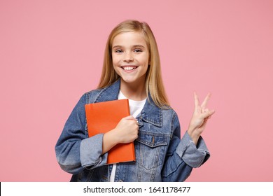 Funny little kid girl 12-13 years old in denim jacket isolated on pastel pink background children portrait. Childhood lifestyle concept. Mock up copy space. Hold book, notebook, showing victory sign