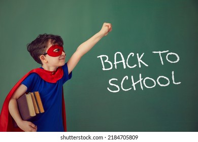 Funny little power super hero child (boy) in a red raincoat. Funny kid against green chalkboard. Idea and creativity and back to school concept. - Shutterstock ID 2184705809