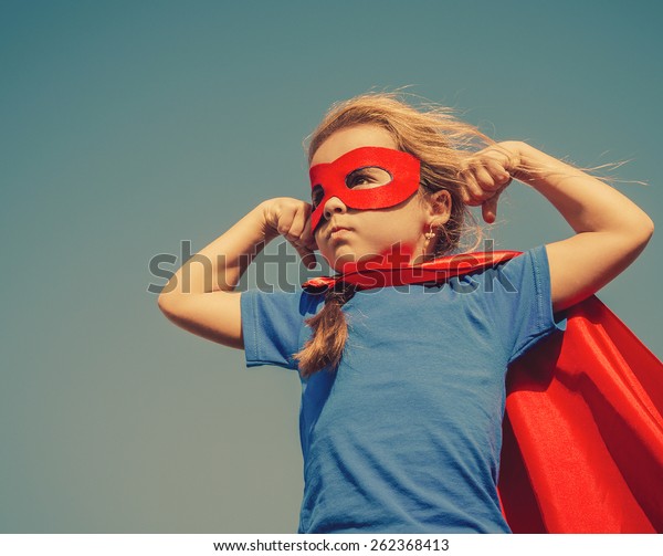 Funny little power super\
hero child (girl) in a red raincoat. Superhero concept. Instagram\
colors toning