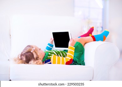 Funny little toddler girl with tablet pc relaxing on a white couch