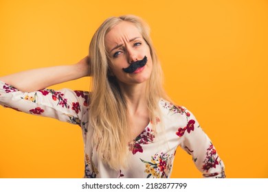 Funny long-haired blond caucasian woman in her mid 20s with fake black moustache on her face. Confused facial expression. Medium closeup studio shot over orange background. High quality photo - Powered by Shutterstock