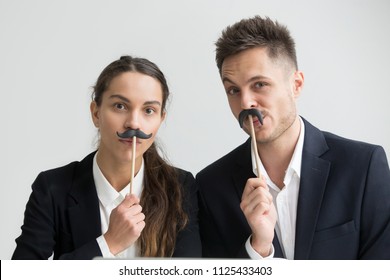 Funny male and female colleagues in suits holding fake mustache, businessman and businesswoman making silly faces, millennial coworkers grimacing looking at camera, creative team head shot portrait - Powered by Shutterstock