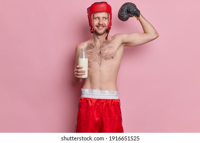 Funny Male Skinny Boxer Raises Arm And Shows Muscles Want To Achieve Great Sport Result Poses With Naked Torso Drinks Milk Wears Protective Helmet And Boxing Glove Isolated On Pink Background