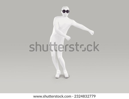 Funny man in bodysuit costume dancing in studio. Full length shot of man disguised in white spandex suit and black round sunglasses doing floss dance isolated on gray background