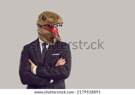 Funny man with dinosaur mask on head with arms crossed symbolizing aggressive and assertive strategy to achieve goals in career or business dressed in formal suit stands on studio background