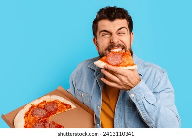 Funny Man Eating Pizza Standing Holding Pizzeria Box Over Blue Background In Studio. Hungry Guy Enjoying Junk Food, Savoring Tasty Unhealthy Meal. Bad Nutrition Habits, Delivery Concept - Powered by Shutterstock