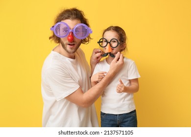 Funny Man And Her Little Daughter In Disguise On Yellow Background. April Fools' Day Celebration