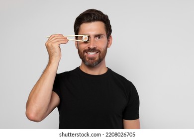 Funny Man Hiding His Eye With Sushi Roll On Light Grey Background. Space For Text