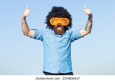 Funny man with large glasses. Funny bearded man with wig and fun glasses on sky background.