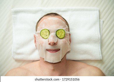 Funny man receiving facial mask of cucumber. Cosmetic procedure man's face. Grooming himself
