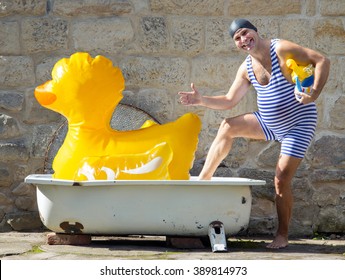 Funny man in retro swimsuit going to the bathtub outdoor. Swimmer in swimming cap goes swimming with inflatable ducks. Childish man bathes with toys.