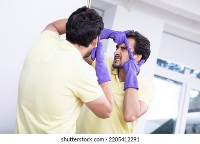 A Funny Man In Rubber Gloves Looks In The Mirror And Diligently Squeezes A Pimple On His Forehead