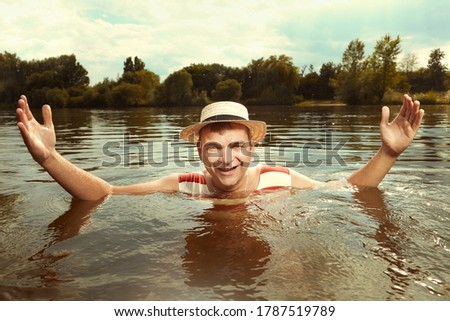 Funny man in stylish retro swimsuit and straw hat swimming in river 