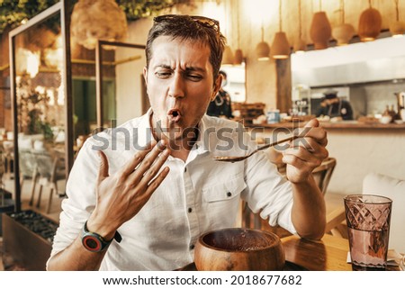 Funny man tries a spicy and hot dish from the national cuisine. He's all red and is trying to cool his mouth with his hand