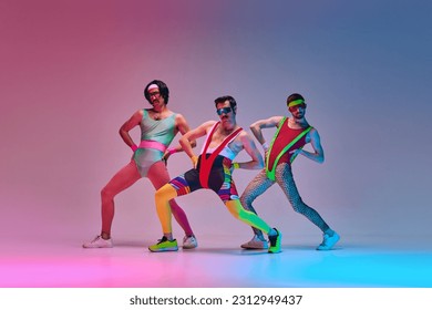 Funny men in vintage, colorful sportswear posing, doing aerobics exercises against gradient blue pink studio background in neon light. Concept of sportive and active lifestyle, humor, retro style. Ad - Shutterstock ID 2312949437