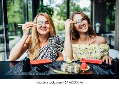 Funny mom with daughter holding sushi rolls in front of eyes and smiling.