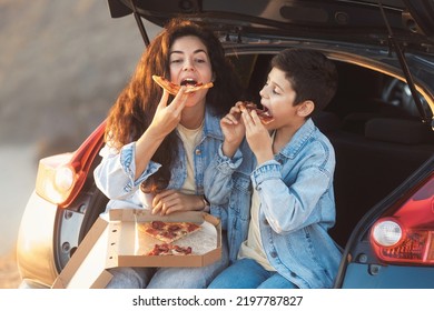 Funny Mom With Teen Son Sitting In The Trunk Of A Car And Eating Slices Of Take Away Pizza From Box. Happy Mother's Day Concept.