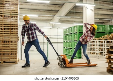 Funny moments on a break at work, a back to childhood. Happy couple behaves unprofessionally in the storage with stock of products. Driving on a hand truck and losing balance. Yellow protective helmet