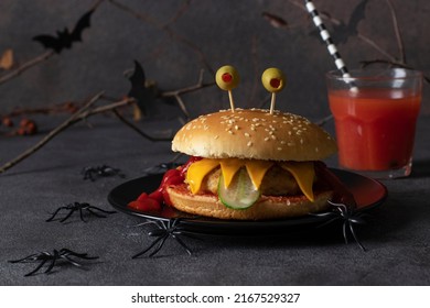Funny monster chicken burger with toast cheese, ketchup, olives and cucumber on dark background. Creative Halloween food