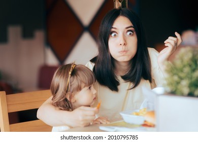 Funny Mother And Daughter Celebrating At Fast Food Birthday Party. Mom Stealing French Fries So Her Child Won’t Eat Junk Food In A Restaurant 
