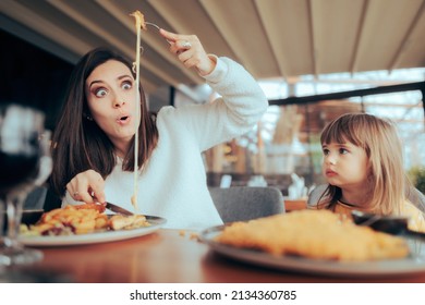 
Funny Mother and Daughter Eating Together in a Restaurant. Mom and girl having fun at the table with cheesy meal 
