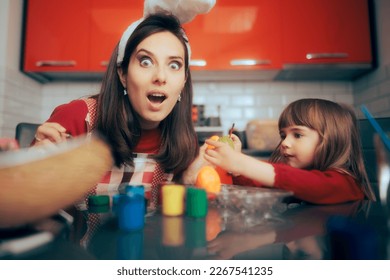 
Funny Mother and Daughter Painting Easter Eggs Together. Happy family decorating eggs for traditional holiday celebration
