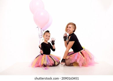 Funny Mother and daughter in same outfits with tutu skirts posing with pink balloons in studio on white background. Little girl and young mom together