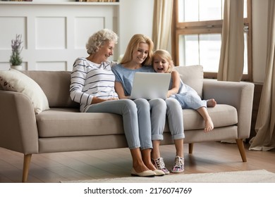 Funny Movie. Happy Family Of 3 Diverse Age Female Members Resting On Sofa At Home With Laptop, Hoary Aged Grandmother, Her Adult Daughter And Small Grandchild Girl Watching Comedy On Computer Screen