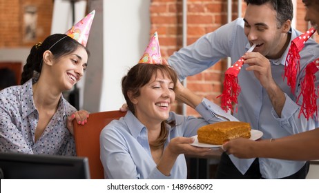 Funny Multiracial Work Team Have Fun Congratulate Smiling Female Colleague Present Tasty Birthday Cake, Excited Diverse Workers Surprise Coworker Make Office Party Celebrating Anniversary At Workplace