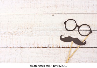 Funny mustache and glasses on sticks against a rustic white wood background. Top view with copy space. Funny mustache and glasses on sticks against a rustic white wood background. Top view with copy space.