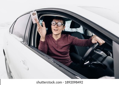 Funny nerd and geek in huge ridiculous glasses shows his drivers license. Concept of police checks on the roads and the correction of vision for drivers