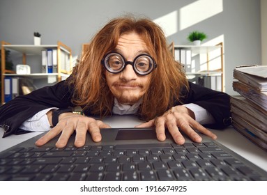 Funny nerd in round thick lens glasses sitting at desk and using laptop. Crazy looking office worker or computer geek typing on keyboard, searching for information on the Internet or doing accounts - Shutterstock ID 1916674925