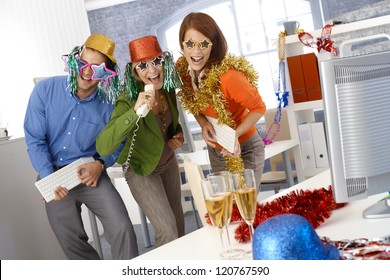 Funny New Year Eve Party In Office, Businesspeople Singing Dancing With Office Tools, Wearing Festive Party Hat And Glasses.