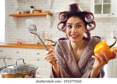 Funny Newbie Housewife Having Trouble In Kitchen. Woman In Bathrobe And Hair Curlers Shrugging Shoulders Not Knowing How To Cook Soup, Feeling Bad, Stressed, Confused, Awkward, Embarrassed, Helpless