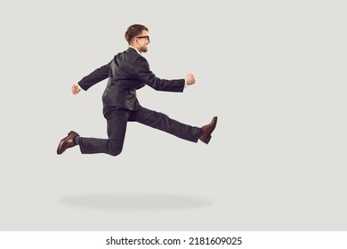 Funny Office Worker Or Business Man Hurrying To Important Work Meeting. Full Body Length Profile View Of Funny Crazy Young Entrepreneur In Suit And Glasses Running Isolated On Solid Grey Background