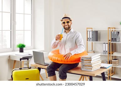 Funny office worker ready to go on summer holiday. Happy smiling man in white shirt, sun hat beach ring and sunglasses drinks orange juice, sitting on desk with laptop and papers. Annual leave concept - Shutterstock ID 2300457029