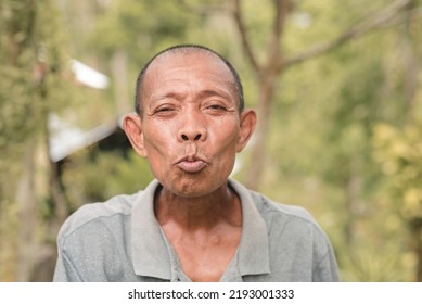 A Funny Old Filipino Man Blows An Imaginary Kiss. Eyes Closed And Puckered Up Lips. Hilarious Outdoor Scene.