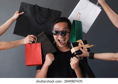 Funny online shopping sales promotion with silly expression shopaholic man by many hands holding shopping bags