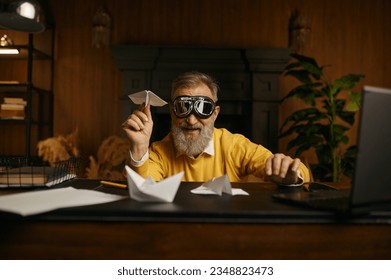 Funny overjoyed mature man wearing pilot goggles playing with origami plane