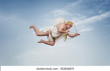 Funny overweight cupid aiming with the arrow of love over clear blue sky with copy space