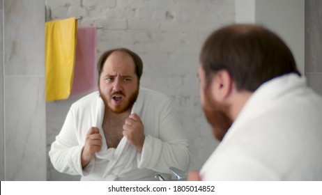 Funny overweight man in bathrobe looking in bathroom mirror and dancing. Cheerful fat guy having fun in home bathroom doing morning routine or preparing for sleep - Powered by Shutterstock