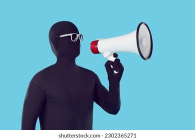 Funny person in bodysuit makes announcement through megaphone. Strange man wearing monochromatic black spandex costume with glasses standing on blue background and talking through loudspeaker