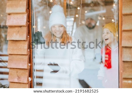 funny photo of family through window in cozy winter house, teenage girl looks out of window at winter snow forest, Christmas and New Year holidays and vacation