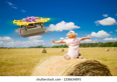 Funny Photo Manipulation Of Drone Delivering Gift Box In Rural Area Countryside, Blurred Field With Hay Balls And Child Hands Reached Out And Doing Fly Move, Sunny Day. Drone Delivery Concept.