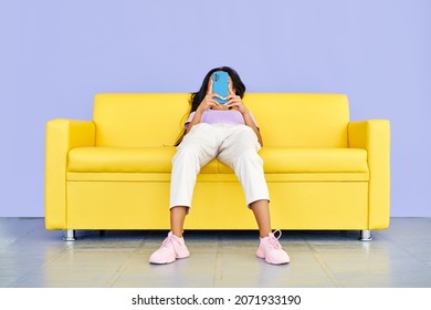 Funny photo of woman types text message on cell phone, enjoys online communication lying on yellow sofa
