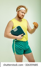 Funny picture of red haired, bearded, plump man on white background.  Man holding a sandwich and scales 
