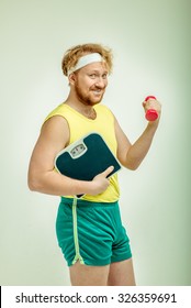 Funny picture of red haired, bearded, plump man on white background.  Man holding a dumbbell and scales 