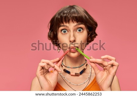 funny pierced girl in her 20s eating two different flavors of sweet and sour candies on pink