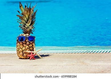 Funny pineapple in sunglasses near swimming pool.