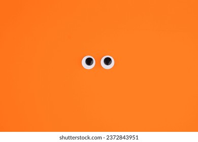 Funny plastic eyes on an orange background. Halloween greeting card 